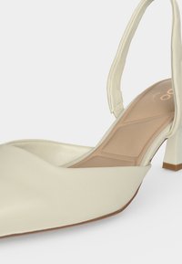 Chaussure slingback à petit talon de couleur crème avec bout pointu et semelle intérieure rembourrée sur fond clair.