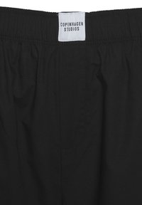 Čierne šortky s elastickým pásom a hladkým povrchom, s malou nálepkou s nápisom "Copenhagen Studios" a bočnou vreckom.