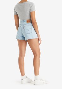 Ljusblå denimshorts med hög midja, fransad fåll och två bakfickor. En fitted grå ribbad topp och vita sneakers kompletterar outfiten.