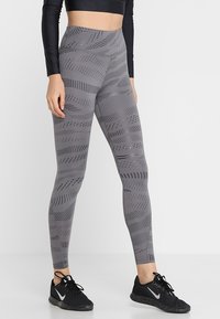 Leggings atletici grigi presentano un motivo a onde e un design testurizzato, a vita alta, realizzati in materiale elastico, abbinati a sneakers nere.