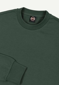 Sweat-shirt à col rond vert foncé avec col et poignets côtelés, arborant une étiquette noire et blanche "Colmar Originals" à l'intérieur de l'encolure.