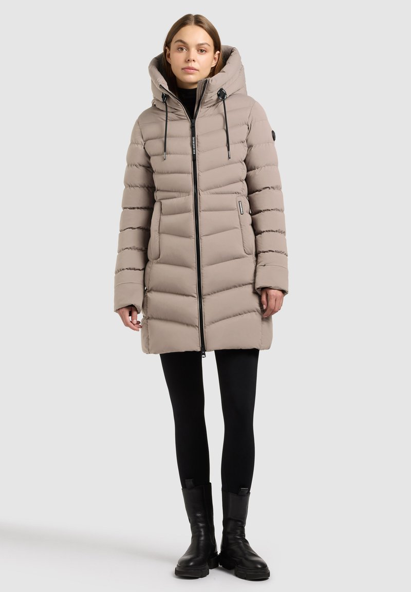 Lichtbeige pufferjas met een capuchon, horizontaal gestikt ontwerp, ritssluiting aan de voorkant en twee zijzakken. Zwarte accenten en een gladde textuur.