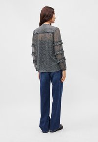 Διαφανής, μπλε πουκάμισο με σχέδιο και φρουφιριστές μανίκες, σε συνδυασμό με φαρδιά σκούρα τζιν. Η μπλούζα διαθέτει στρογγυλή λαιμόκοψη και υφή.