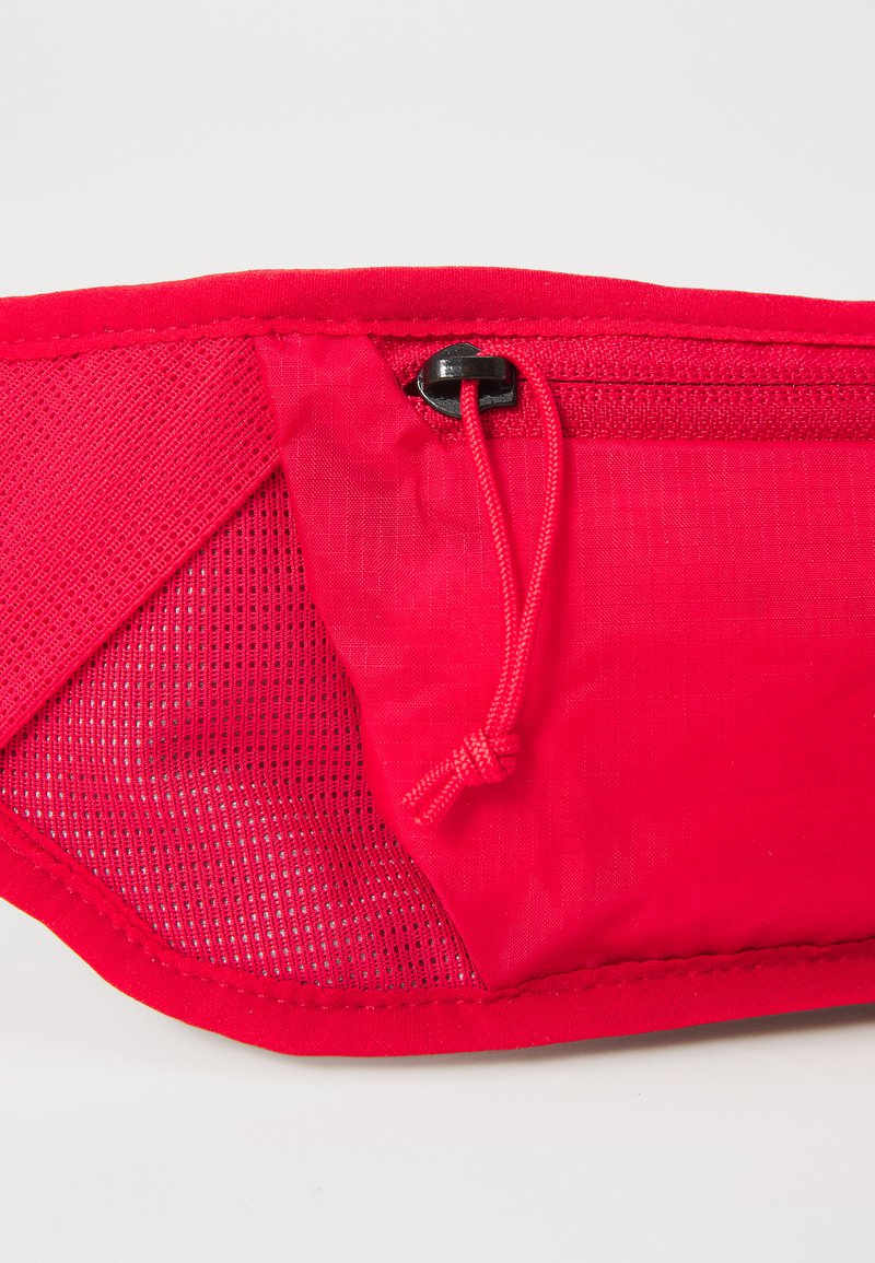 Bolsita de tela roja con un panel de malla texturizada, cordón ajustable y compartimento con cremallera. Cuenta con costuras reforzadas para mayor durabilidad.