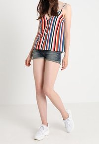 Raidallinen hihaton toppi v-kauluksella ja etunapeilla, yhdistetty farkkushortseihin. Kangas näyttää eloisia punaisen, sinisen, vihreän ja keltaisen raitoja.