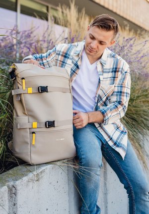 Beige backpack with adjustable straps and yellow accents. Smooth material, roll-top design, features a zippered front pocket.