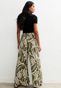 Wide-leg trousers made of lightweight fabric, featuring a leaf pattern in green and beige. Elastic waistband for comfort.