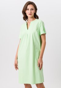Lichtgroene jurk met korte mouwen, een V-hals, getailleerde pasvorm, minimale stikdetails en een zoom tot op de knie. Gladde, katoenachtige textuur.