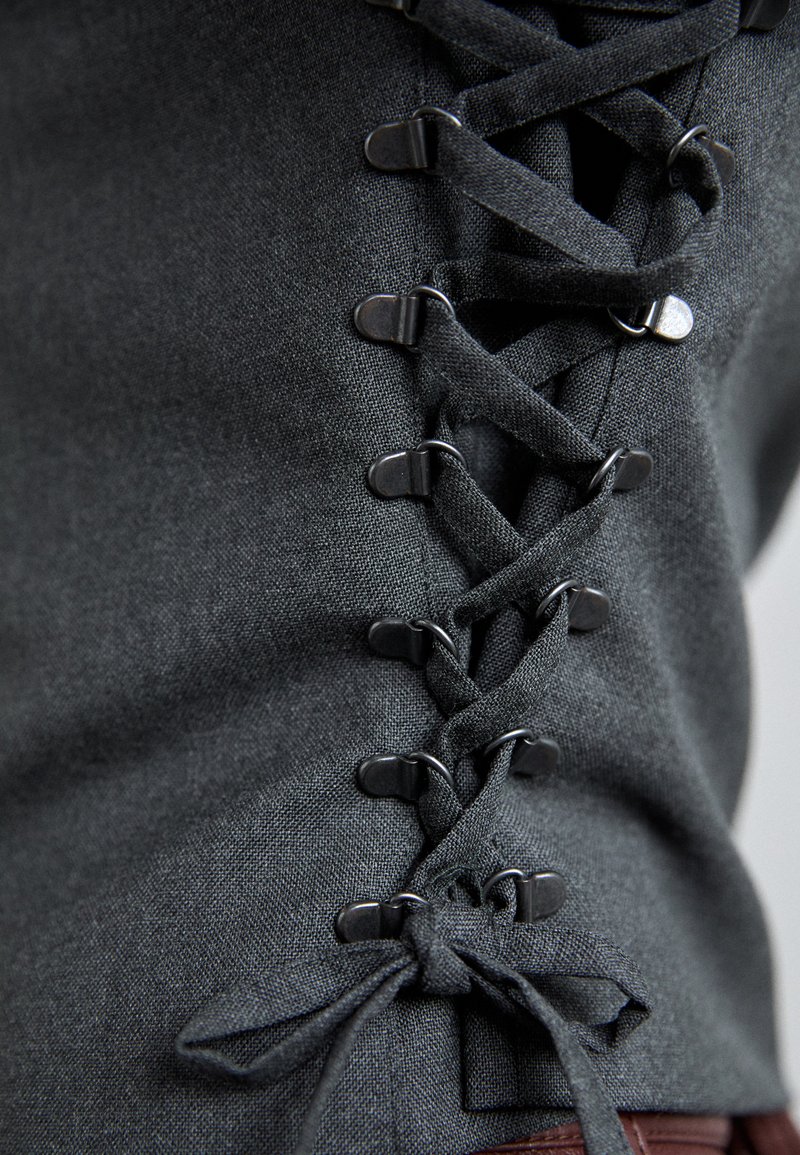 Tessuto nero con una finitura testurizzata, caratterizzato da un design con lacci e occhielli in metallo sui lati per una vestibilità regolabile.