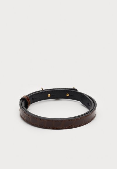 Bruin leren armband met een gladde afwerking, voorzien van gouden hardware accenten en een drukknoopsluiting. Platte bandontwerp met een gepolijste textuur.