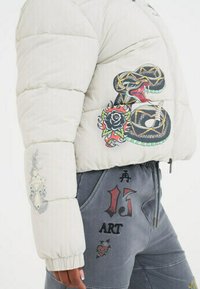 Giacca a vento bianca e pantaloni grigi con decorazioni ricamate colorate di un serpente, una rosa, un pugnale e disegni di testo sui lati e sulle maniche.