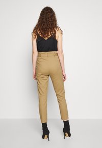 Khaki kalhoty s vysokým pasem a zúženou nohavicí, spárované s černým tílkem. Tento outfit se vyznačuje hladkou texturou a přiléhavým střihem.