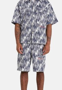 Korte mouwen overhemd en shorts in een marineblauw en wit abstract patroon. Knopsluiting aan de voorkant, twee borstzakken en rode logo-details. Katoenen stof.