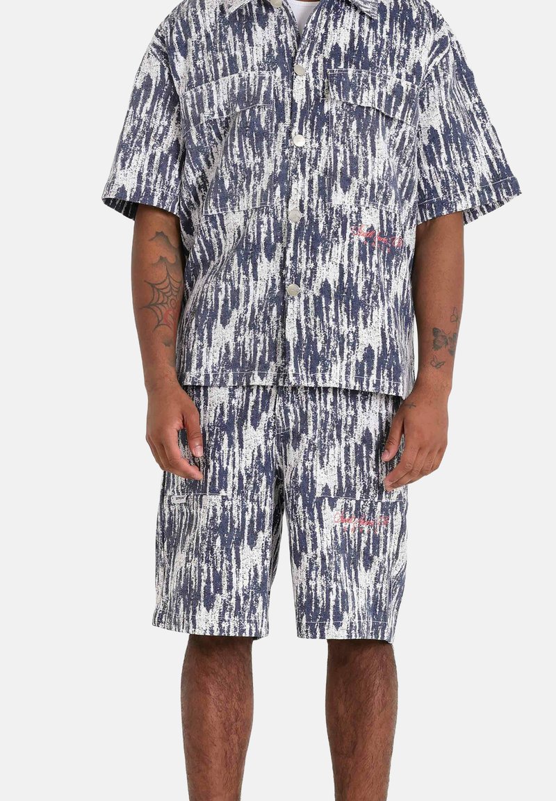 Korte mouwen overhemd en shorts in een marineblauw en wit abstract patroon. Knopsluiting aan de voorkant, twee borstzakken en rode logo-details. Katoenen stof.