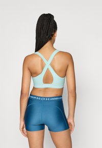 Ανοιχτό μπλε αθλητικό σουτιέν με σχεδιασμό σταυρωτής πλάτης, συνδυασμένο με σκούρο μπλε εφαρμοστά σορτς με φαρδύ ελαστικό μέση με λογότυπο. Ομαλή υφή.