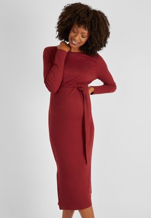 Ribbed long-sleeve dress in burgundy, featuring a fitted silhouette and a tie detail at the waist. Smooth texture and mid-length cut.