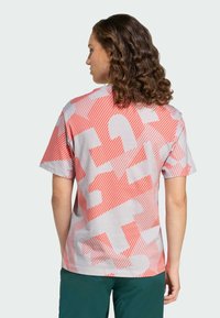 Koszulka z krótkim rękawem w jasnoszarym kolorze z dużym, czerwono-białym, abstrakcyjnym wzorem. Materiał to miękka bawełna o swobodnym kroju.