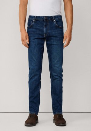 Mörkblå denimjeans med smal passform, femficksdesign och subtilt blekt mönster, kombinerat med bruna snörskor.