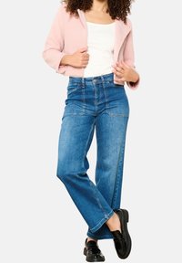 Niebieskie dżinsy z wysokim stanem o luźnym, szerokim kroju nogawek i kontrastującymi przeszyciami. W połączeniu z jasnoróżową, teksturowaną kurtką.
