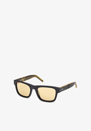 Occhiali da sole neri quadrati con lenti giallo-tintate, finitura opaca e aste con accenti dorati caratterizzate da sottili dettagli a righe.