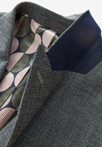 Blazer grigio intrecciato con tessuto testurizzato, colletto blu e foderatura con motivo geometrico multicolore in tonalità di verde, blu navy e rosa.