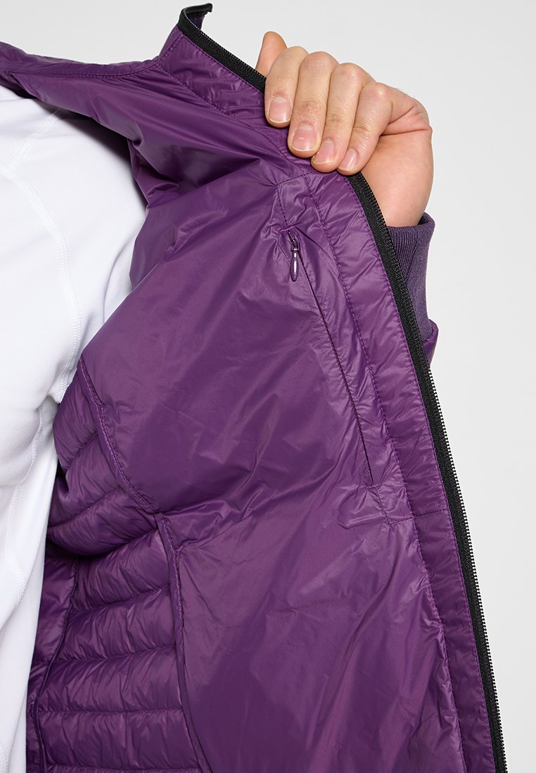 Innenseite einer lila isolierten Jacke mit gestepptem Muster, Reißverschlusstasche und schwarzem Reißverschlussrand. Glatter, leichter Stoff.