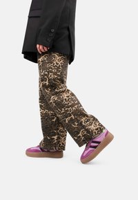 Pantalons à imprimé léopard en beige et marron, associés à des baskets violettes et noires avec une surface texturée et une semelle contrastante. Blazer noir.