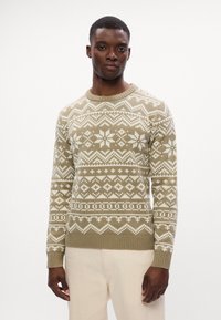 Sweter dzianinowy w jasnym oliwkowym kolorze z białymi geometrycznymi i śnieżynkowymi wzorami. Posiada okrągły dekolt oraz ściągacze na mankietach i u dołu. Gładka struktura.