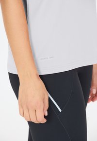 Ljusgrå snabbtorkande topp med korta ärmar, med en mjuk textur. En svart leggings med slim fit och en subtil blå accentrand.