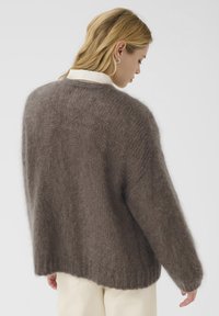 Brun, överdimensionerad tröja gjord av mjukt, texturerat material; har ribbade manschetter och fåll, med en lätt sänkt axeldesign.