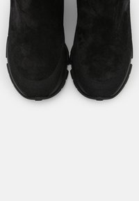 Botines de ante negro con una superficie texturizada, punta redonda y suela de goma negra para mayor tracción. Diseño sencillo sin elementos metálicos visibles.