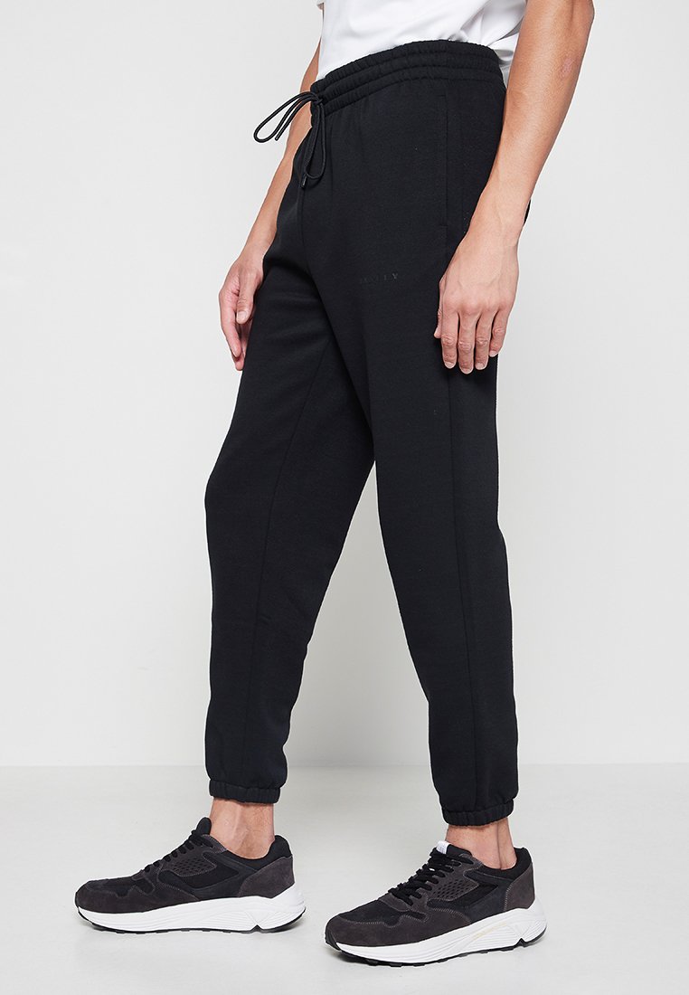 Czarne spodnie dresowe wykonane z miękkiego materiału, z elastycznym pasem ze sznurkiem, zakończone ściągaczem przy kostkach oraz dwoma bocznymi kieszeniami.