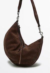 Hnědá semišová kabelka přes rameno ve tvaru půlměsíce, vybavená zipem a látkovým popruhem s kovovými ozdobnými prvky.