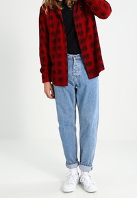 Czerwona i czarna koszula w kratę zapinana na guziki, noszona na czarnym topie, zestawiona z jasnoniebieskimi prostymi d�żinsami i białymi trampkami.