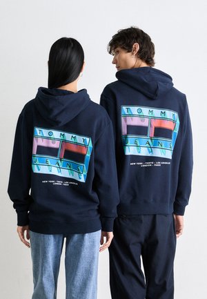 Marineblauwe hoodies met een grafisch ontwerp dat "TOMMY JEANS" leest. Opmerkelijke kenmerken zijn een gladde textuur en een relaxte pasvorm.