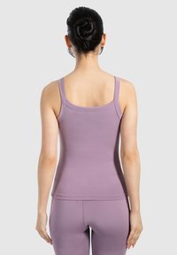 Top in lavanda con spalline sottili, design aderente e texture liscia. Indossato con leggings abbinati in lavanda, visto da dietro.