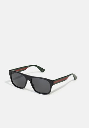 Óculos de sol pretos com armação retangular, lentes cinzentas e hastes verdes com riscas vermelhas. Logótipo gravado nas hastes.