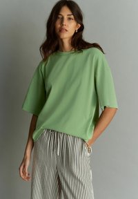 Camiseta oversized verde claro con mangas cortas, combinada con pantalones a rayas en blanco y negro. Textura suave y ajuste relajado.