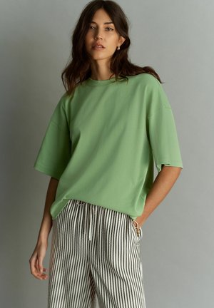Lichtgroene oversized t-shirt met korte mouwen, gecombineerd met zwart-wit gestreepte broek. Zachte textuur en een relaxte pasvorm.