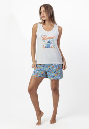 Mujer con camiseta sin mangas gris con la inscripción "Saludos desde Hawái" y un personaje de dibujos animados, combinada con pantalones cortos azules con estampado con un personaje similar.