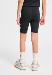 Grå idrottsshorts gjorda av ett slätt, stretchigt material, med en vit randdetalj på vänster sida, i kombination med grå skor och vita strumpor.