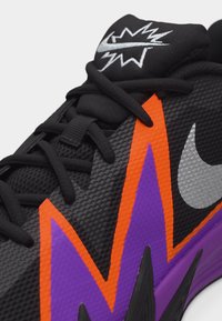 Pantof sport texturat negru cu design zigzag mov și portocaliu, șireturi negre, logoul Nike argintiu și grafică argintie pe limba neagră.