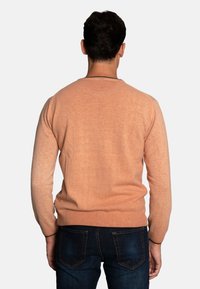Licht perzikkleurige gebreide trui met lange mouwen en een ronde halslijn, met een soepele textuur en ribbels aan de mouwen en onderkant. Draag met donkerblauwe jeans.