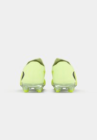 Cizme de fotbal galbene cu un design elegant, având o limbă verde, accente negre și prelungiri transparente pentru aderență pe teren.
