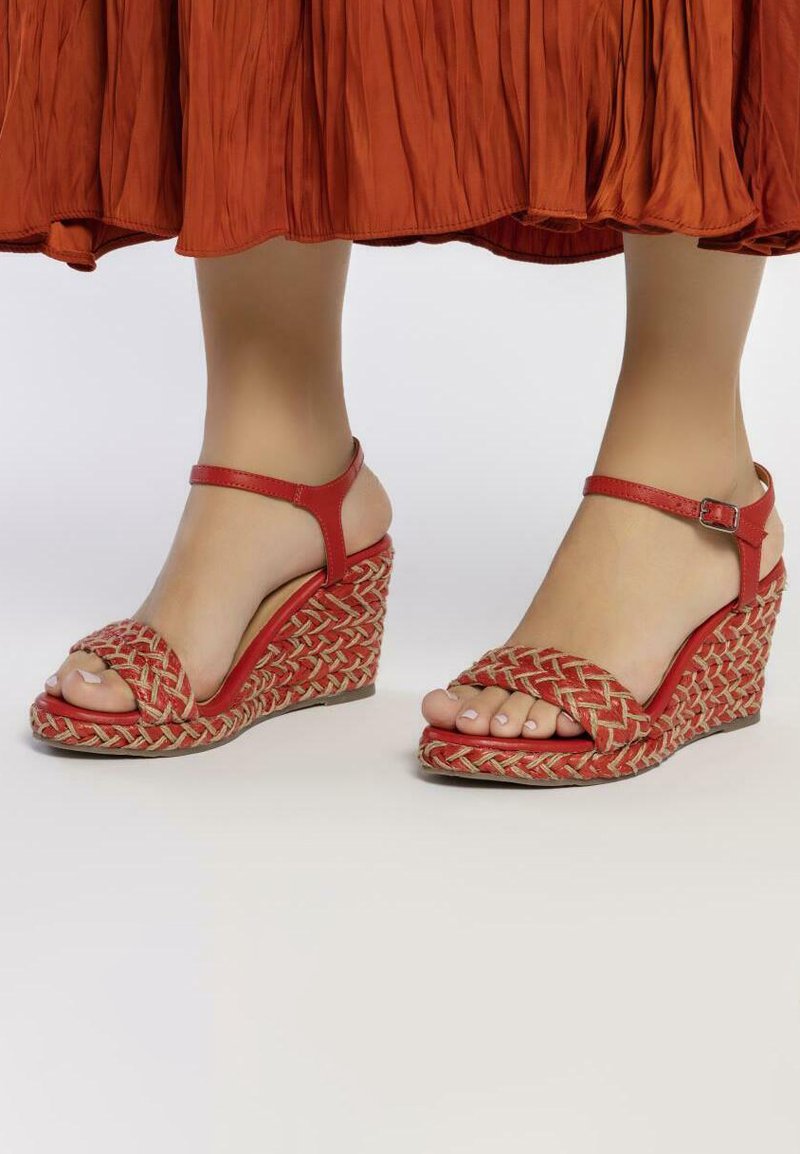 Sandalias de cuña tejidas rojas con un diseño trenzado texturizado. Presentan una delgada correa en el tobillo y la parte delantera abierta, con un tacón de cuña de tono natural.