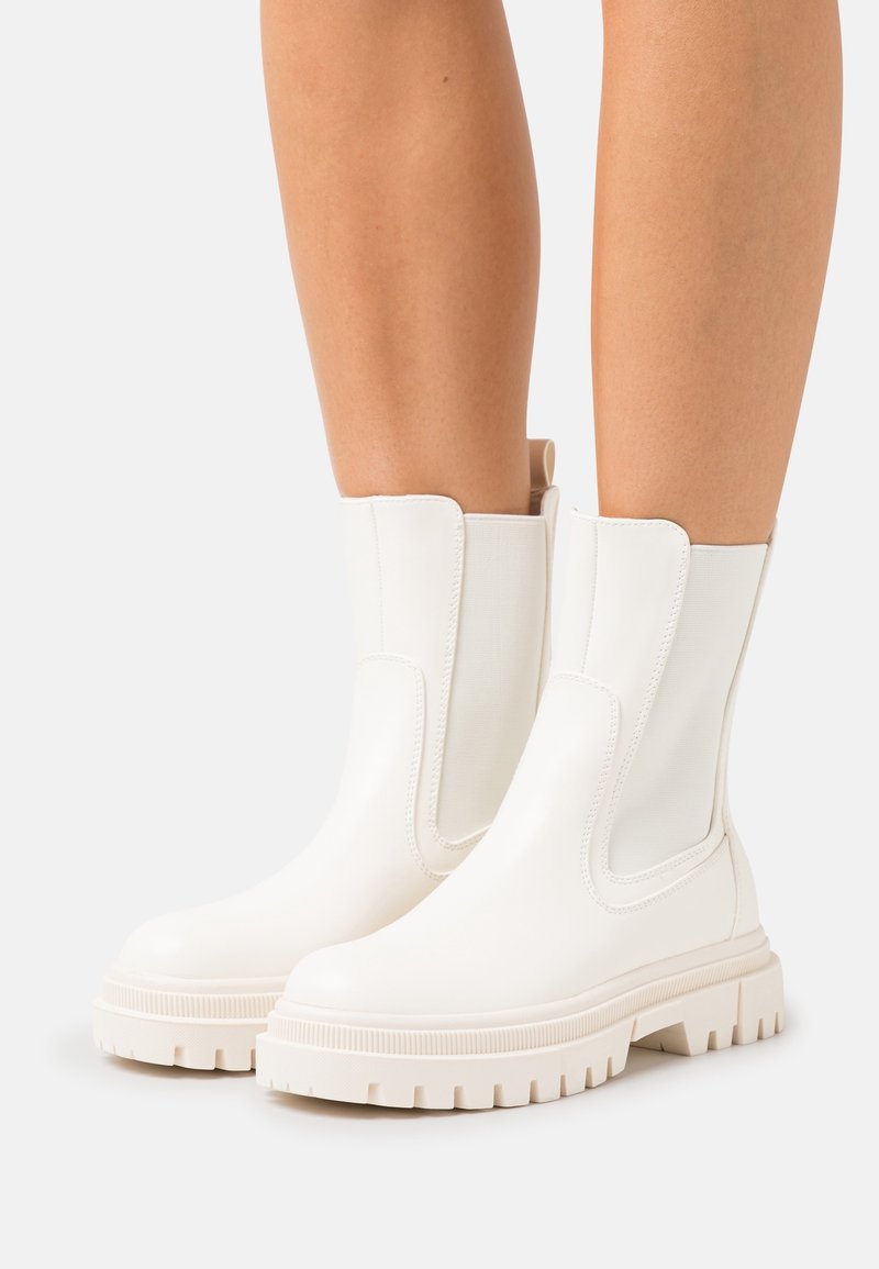 Bottines blanches à finition mate, avec des panneaux latéraux élastiques et des semelles en caoutchouc épaisses dotées de profondes rainures pour une meilleure adhérence.