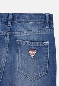 Jeans aus Denim mit hohem Bund, hellblauer Farbe und einem roten Dreiecks-Patch mit weißem Text auf der Gesäßtasche.