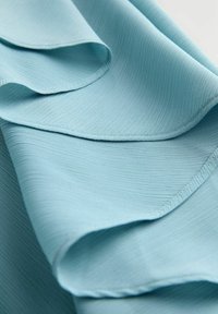 Tela azul claro con una textura acanalada y pliegues suaves y fluidos. Presenta bordes lisos y una apariencia ligera, ideal para drapear.