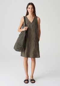 Olive green sleeveless dress with textured leaf pattern, paired with a woven bag and black sandals, featuring a V-neck design.