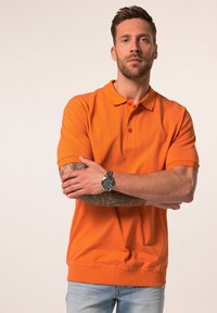 Orange polo skjorta med klassisk krage, korta ärmar och en subtil logga. Tyget verkar slätt och något texturerat.